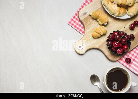 Frühstück mit hausgemachten Croissants, Kaffee und Süßkirschen auf hellem texturierten Hintergrund, Draufsicht mit Kopierraum. Stockfoto