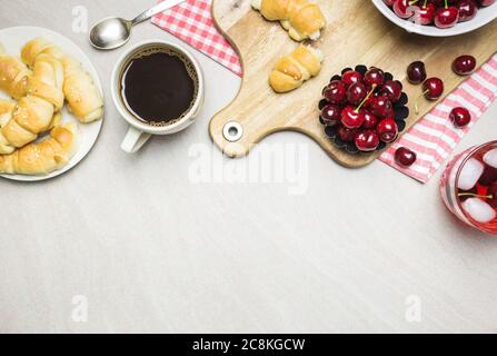 Frühstück mit hausgemachten Croissants, Kaffee, Saft und Süßkirschen auf hellem texturierten Hintergrund, Draufsicht mit Kopierraum. Stockfoto