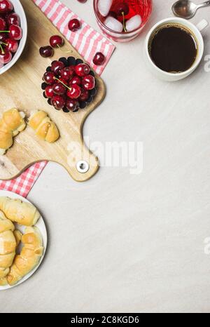 Frühstück mit hausgemachten Croissants, Kaffee, Saft und Süßkirschen auf hellem texturierten Hintergrund, Draufsicht mit Kopierraum. Stockfoto