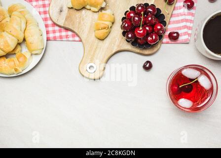 Frühstück mit hausgemachten Croissants, Kaffee, Saft und Süßkirschen auf hellem texturierten Hintergrund, Draufsicht mit Kopierraum. Stockfoto