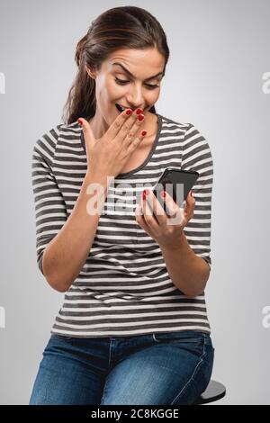 Schöne Frau auf einer Bank sitzt erstaunt über eine Nachricht empfangen Stockfoto