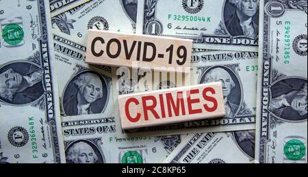 'Covid-19 Crimes' Worte auf Holzblöcken. Geschäftskonzept. Schöner Hintergrund von Dollarscheinen. Stockfoto