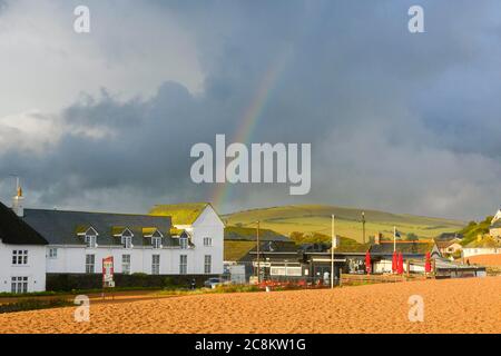 West Bay, Dorset, Großbritannien. Juli 2020. Wetter in Großbritannien. Die Sonne scheint nach heftigen Regenschauern klar mit einem Regenbogen über den Strandhütten am Badeort West Bay in Dorset. Bildquelle: Graham Hunt/Alamy Live News Stockfoto