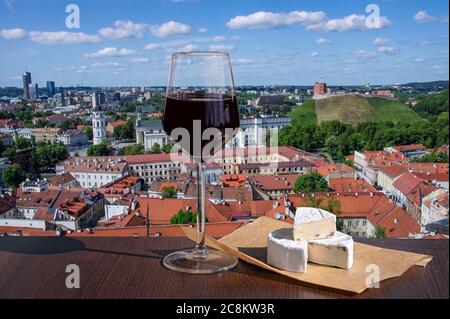 Glas Rotwein mit Brie-Käse mit Blick auf die St. Stanislaus Kathedrale auf dem Domplatz, Gediminas Schloss auf dem Hügel, rote Dächer in Vilnius Stockfoto