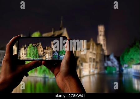 Tourist Foto von Kanal von Brügge, Turm und historischen Gebäuden bei Nacht, Brügge, Belgien. Mann, der Telefon hält und fotografiert. Stockfoto