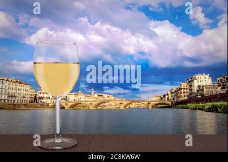 Ein Glas Weißwein mit Blick auf die Brücke in Florenz während des Sonnenuntergangs - Ponte alla Carraia, fünfbogenige Brücke über den Fluss Arno in der Toskana Stockfoto