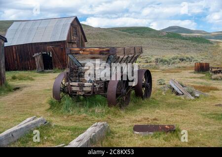 Verlassene Holzscheune und Holzanhänger in einem Grasfeld. Stockfoto