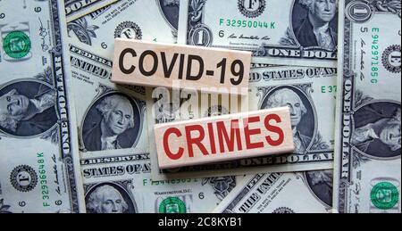 'Covid-19 Crimes' Worte auf Holzblöcken. Geschäftskonzept. Schöner Hintergrund von Dollarscheinen. Stockfoto