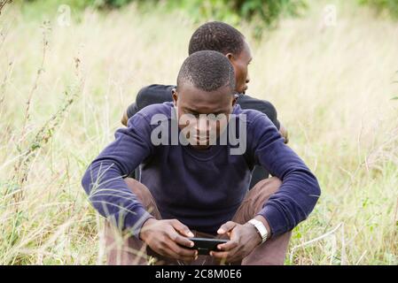 Nahaufnahme von zwei jungen Männern, die sich anlehnen und auf dem Gras im Park sitzen. Einer von hinten gesehen und der andere von vorne gesehen benutzt Stockfoto