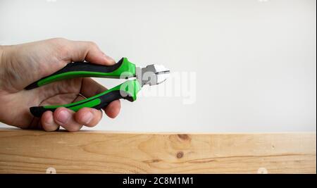 Eine männliche Hand hält einen Drahtschneider an einer Holzstange. Schöner weißer Hintergrund. Speicherplatz kopieren. Stockfoto