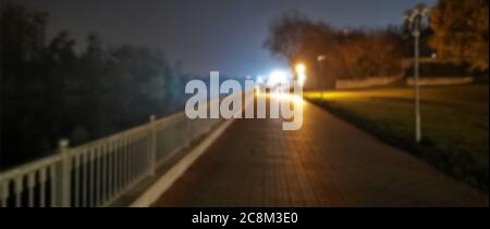 Blick auf die Steinbrücke über den Fluss bei Nacht mit Lichtstrahlen und Reflexionen. Verschwommenes Bild. Stockfoto