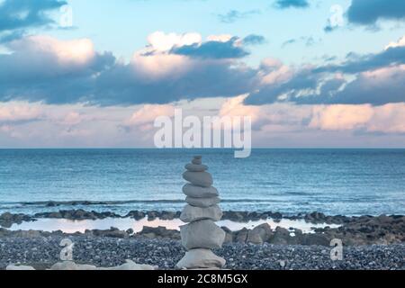 Ein Haufen Zen-Felsen an einem Kiesstrand in Sussex, mit dem Ozean dahinter und einem Abendhimmel über dem Meer Stockfoto