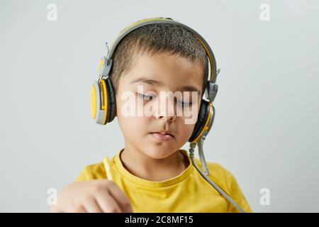 Nachdenkliches Schuljunge Porträt. Kopfbild eines Jungen mit 6 bis 7 Jahren in gelbem T-Shirt, Brille und Kopfhörer Stockfoto