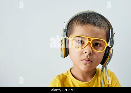 Nachdenkliches Schuljunge Porträt. Kopfbild eines Jungen mit 6 bis 7 Jahren in gelbem T-Shirt, Brille und Kopfhörer Stockfoto