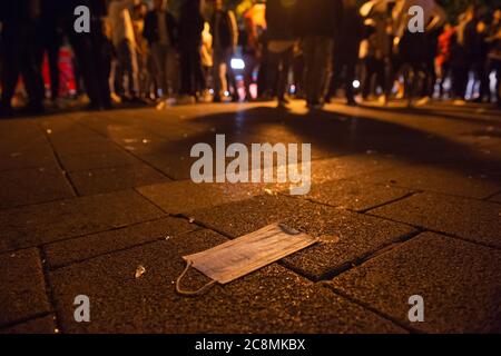 Hamburg, Deutschland. Juli 2020. Ein Mundschutz liegt auf dem Bürgersteig am Schulterblatt, während Dutzende von Menschen im Hintergrund stehen. Auch in der Nacht zum Sonntag feierten viele Menschen im Schanzenviertel und auf St. Pauli ohne die Regeln der Ferne zu beachten. Manchmal musste die Polizei den Zugang zur Großen Freiheit sperren, weil die Straße überfüllt war. Quelle: Jonas Walzberg/dpa/Alamy Live News Stockfoto