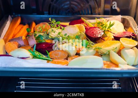 Schneiden Sie rohes Gemüse, bevor Sie es in den Ofen stellen. Karotten, Kartoffeln, Süßkartoffeln, Rüben, Kohlrabi, Rosmarin, Knoblauch, Ysop Stockfoto