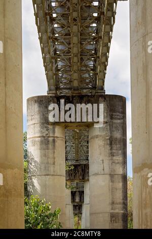 Eine Eisenbahnbrücke, die von unten zwischen zwei Betonstützpfosten eingerahmt ist Stockfoto