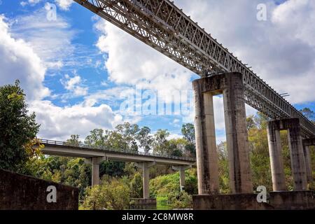 Eine Eisenbahnbrücke aus Beton und Stahl über einem Landfluss gegen einen wolkigen blauen Himmel Stockfoto
