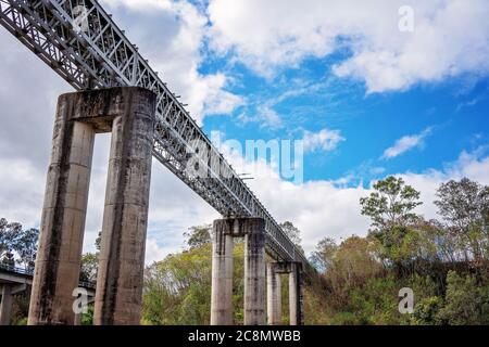 Eine Eisenbahnbrücke aus Beton und Stahl über einem Landfluss gegen einen wolkigen blauen Himmel Stockfoto
