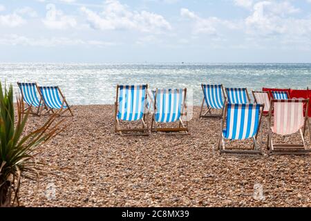 Bunt gestreifte leere Liegestühle zu vermieten am Kiesstrand in Brighton, East Sussex, England Stockfoto