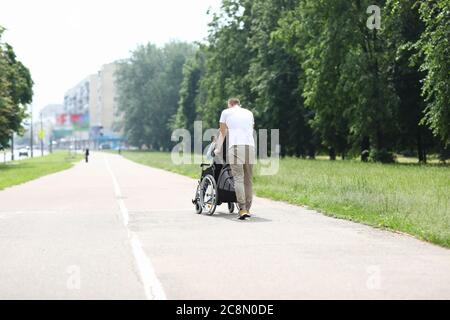 Mann läuft mit Frau im Rollstuhl im Park. Stockfoto