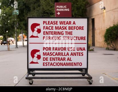 Schild mit der Aufschrift: "Bitte tragen Sie eine Gesichtsmaske, bevor Sie die Parkgarage betreten", außerhalb einer öffentlichen Garage in Downtown Los Angeles, Kalifornien. Stockfoto