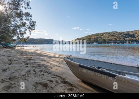 Ein kleines legiertes Boot (Dinghy) oder Tinnie sitzt am späten Nachmittag auf dem Sand neben dem ruhigen Wasser von Pittwater am Church Point in Sydney, Australien Stockfoto