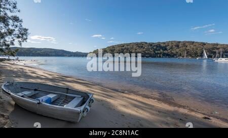 Ein kleines legiertes Boot (Dinghy) oder Tinnie sitzt am späten Nachmittag auf dem Sand neben dem ruhigen Wasser von Pittwater am Church Point in Sydney, Australien Stockfoto