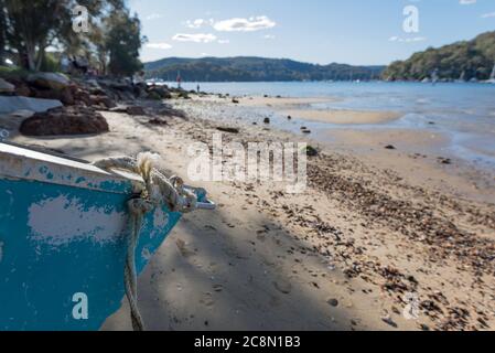 Ein kleines legiertes Boot (Dinghy) oder Tinnie sitzt am späten Nachmittag auf dem Sand neben dem ruhigen Wasser von Pittwater am Church Point in Sydney, Australien Stockfoto