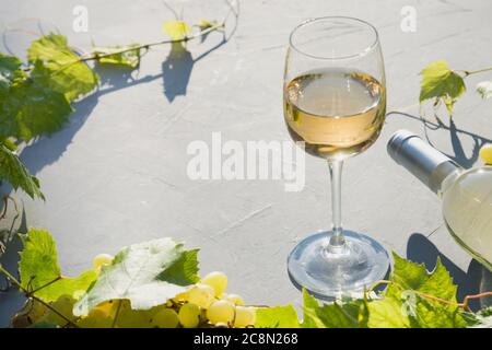 Flasche Weißwein mit Weinglas, reife Trauben auf betongrauem Tisch. Stockfoto