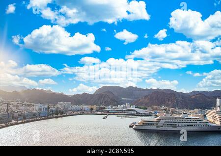 Luftaufnahme des Muttrah Hafens und der Berge in der Ferne mit Schiffen, die an einem hellen sonnigen Abend am Hafen angedockt sind. Stockfoto