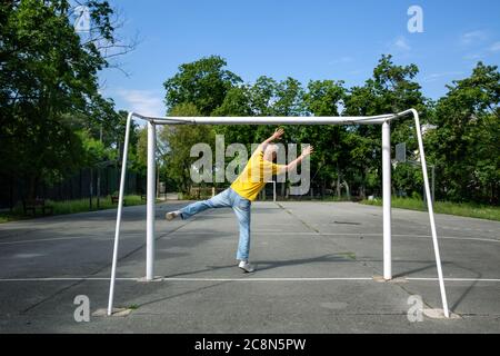 Ein grauhaariger Mann fängt einen imaginären Ball in einem Fußballtor Stockfoto