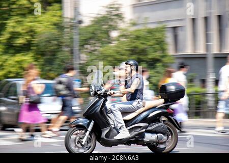 Belgrad, Serbien - 16. Juli 2020: Reifer tätowierte Mann, der im Stadtverkehr auf einem Motorroller mit dem Motorrad unterwegs ist, an der Kreuzung mit Menschen, die vorbei gehen Stockfoto
