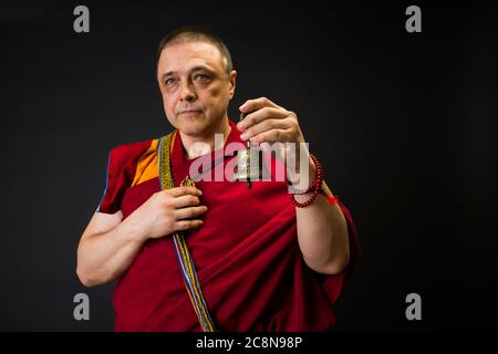 Der Mönch hält eine Gebetstrommel in der Hand. Porträt eines buddhistischen Mönchs in roten Kleidern. Stockfoto