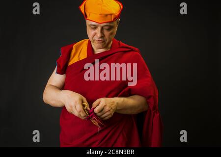 Träger eines buddhistischen Mönchs in einem Lama-Kleid. Der Mönch hält die rituellen Attribute des Buddhismus, Rosenkranz, Vajra, Glocke Stockfoto