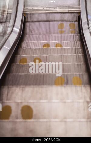 Fußpunkt-Druckschild auf Rolltreppe in gelb, um Abstand während der Covid-19 Pandemie, Gesundheitswesen, Stockfoto