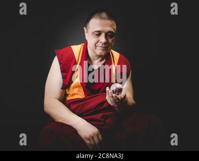 Uddhistischer Mönch in rotem Kleid, einen Kristall aus Glas in der Hand haltend Stockfoto