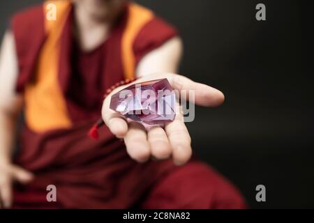 Uddhistischer Mönch in rotem Kleid, einen Kristall aus Glas in der Hand haltend Stockfoto