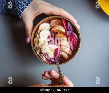 Acai Smoothie, Müsli, Samen, frische Früchte in einer Holzschale in weiblichen Händen auf einem grauen Tisch. Essen gesunde Frühstückschale. Draufsicht Stockfoto