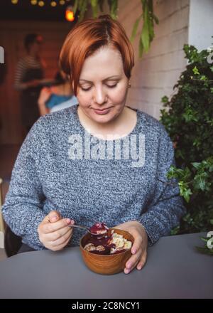 Acai Smoothie, Müsli, Samen, frische Früchte in einer Holzschale in weiblichen Händen auf einem grauen Tisch. Essen gesunde Frühstückschale Stockfoto