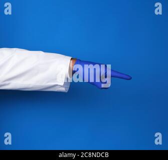 medic in weißem Mantel, trägt in blauen sterilen Handschuhen, zeigt Handbewegung, die das Motiv anzeigt, blauer Hintergrund Stockfoto