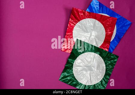 Drei quadratische Stücke von farbigen Folie auf lila Hintergrund. Die Folienstücke sind rot, blau und grün mit einem weißen Kreis. Abstrakter Hintergrund. Flach liegend. Stockfoto