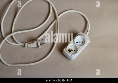 Elektrischer Stecker Zustand, Steckdose nach Schock auf braunem Hintergrund. Weiße Steckdosenleiste nach Kurzschluss. Elektrische Sicherheit. Stockfoto