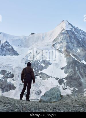 Rückansicht Momentaufnahme eines Touristen, der einen der schönsten Berge der Schweizer Alpen betrachtet - das Ober Gabelhorn, das auf einer Seite mit Schnee bedeckt ist. Trekking, Bergwandern, Mann erreicht Gipfel. Stockfoto