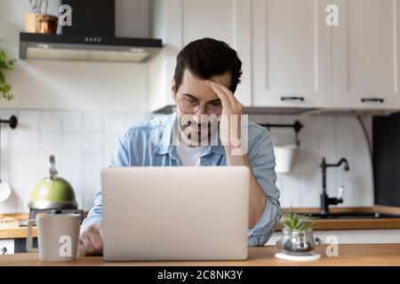 Unglücklicher junger Mann, der über E-Mail auf dem Laptop beunruhigt war Stockfoto