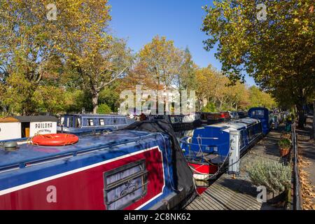 Kanalboote in einer farbenfrohen Herbstszene mit einem lebendigen blauen Himmel entlang des von Bäumen gesäumten Kanals in Little Venice, West London. Stockfoto