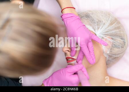 Kosmetologie Schrank Client liegt auf Couch. Kosmetikerin trägt Markierung auf Lippen. Vorbereitung für das Verfahren der permanenten Lippen Make-up. Nahaufnahme. Kosmetikindustrie Stockfoto