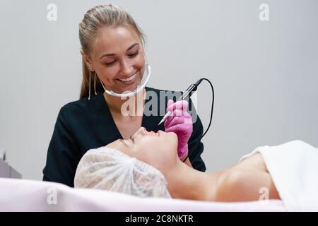 Kosmetologie Kabinett Client liegt auf der Couch. Kosmetikerin gilt permanente Tinte auf die Lippen. Verfahren der permanenten Lippen Make-up. Freien Speicherplatz. Schönheit Industrie Stockfoto