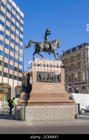 Statue des Prinzen Albert, der seinen Hut (Holborn Circus) gegen den blauen Himmel hebt, mit Inschrift und Tafel, die auf dem roten Granitsockel deutlich sichtbar ist. Stockfoto