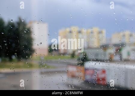 Abstrakter Hintergrund von Regentropfen auf Glas auf dem Hintergrund der Straße und Stadthäuser Stockfoto